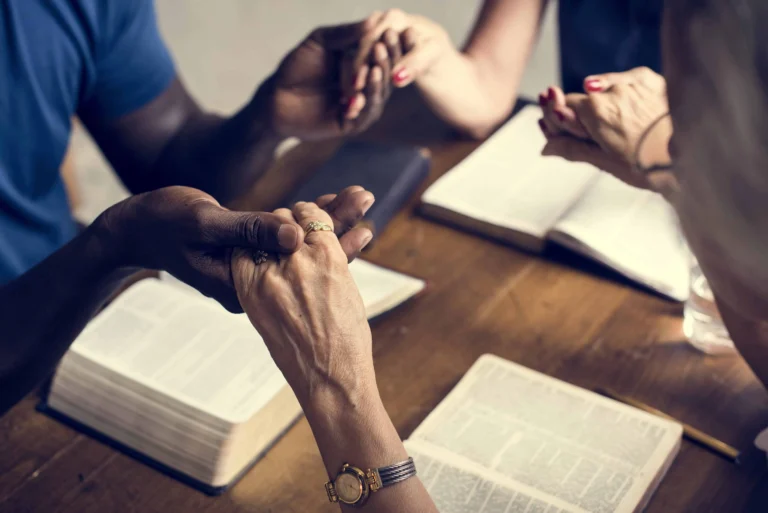 Corporate Prayer 3 people holding hands at a table with bibles open